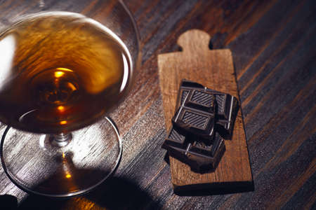 Glass of brandy on a wooden table with chocolate and cigar. gray background.の写真素材