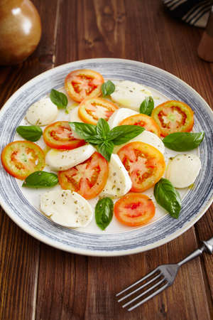 Caprese salad in a blue pastel plate on an old wooden table, with salt and pepper の写真素材