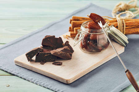 Chocolate, date fruit and cinnamon on a white chopping board on a blue table. Pastel colorsの写真素材