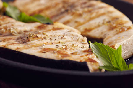 grilled swordfish slices in a cast iron pan on a wooden table, garnished with mint, oregano, salt and salmoriglio の写真素材