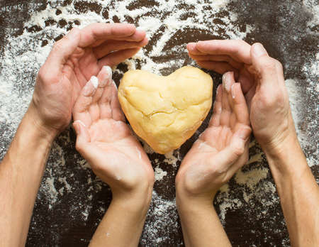 Hands of men and women make dough heart. The symbols of protection, warmth and comfort. Baking lovers on Valentine's Dayの写真素材