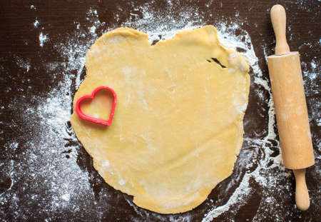 Roll out the dough on a black table. The dough is squeezed out in the shape of a heart for the love of cookiesの写真素材