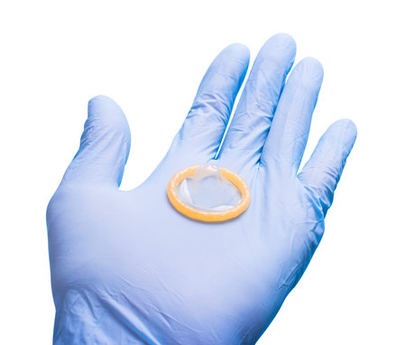 Hand in glove holding a condom. Doctor and contraceptives. White isolatedの写真素材