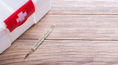 Medical mercury thermometer on a wooden table. First-aid kit with a white cross
