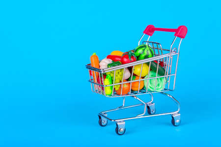 Metal shopping cart with fruits and vegetables on a blue backgroundの写真素材