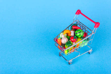 Metal shopping cart with fruits and vegetables on a blue backgroundの写真素材