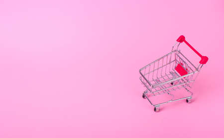 Empty shopping cart with the red handle on a pink backgroundの写真素材
