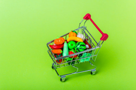 Metal shopping cart with fruits and vegetables on a green backgroundの写真素材