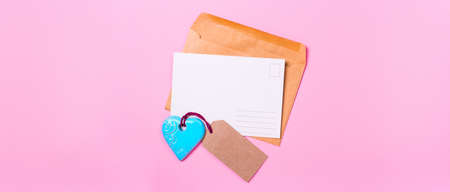 empty postcard love letter with envelope and blue turquoise heart on a pink backgroundの写真素材