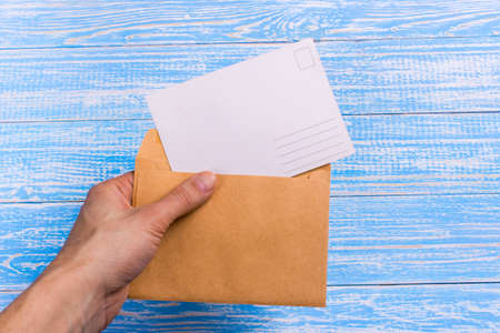 Hand holding a blank postcard and envelope on a blue wooden backgroundの写真素材