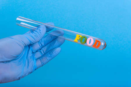Word food of colored wooden letters in test-tube. Hand in glove holding a test tube on a blue backgroundの写真素材