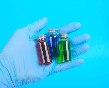 vial with a vaccine or cure for holding a blue gloves on a blue backgroundの写真素材