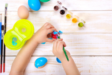 Happy easter. A mother and kid painting Easter eggs. Top view on white wooden tableの写真素材