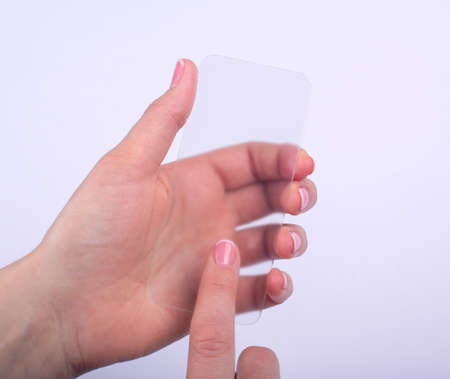 transparent glass phone in a female hand on a gray backgroundの写真素材