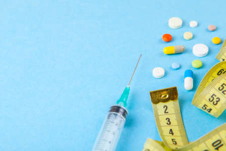 Injections for body beauty and weight loss. Tablets, syringe and yellow measuring tape.の写真素材