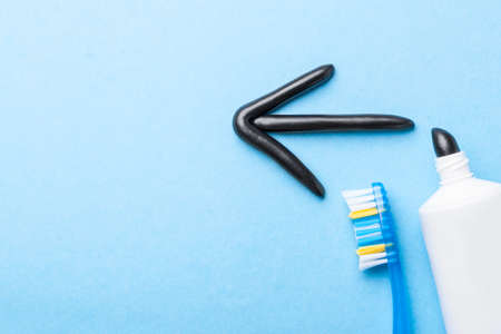 Black toothpaste from charcoal for white teeth. Toothpaste in the form of an arrow to the left,  tube and  toothbrush on  blue background.の写真素材