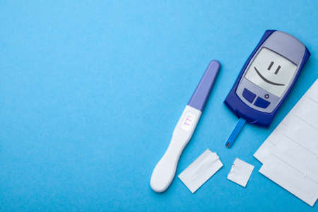 Diabetes mellitus, increased blood sugar in pregnant women. Glucometer and positive test for variability. Smiling face on display. Blue background. Copy space for textの写真素材