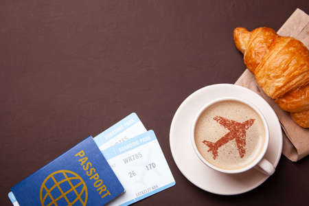 Mug of coffee with an airplane on the foam. I like to break coffee with croissant in flight. Paspor and ticket with smrtrfonom and cup of coffeeの写真素材