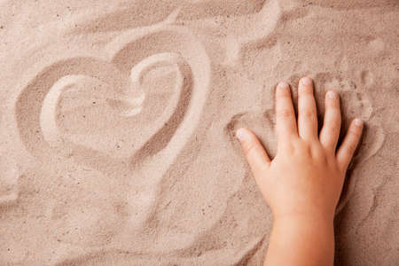 Heart on the sand drawn with child's handの写真素材