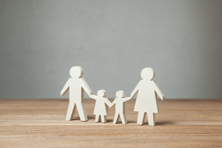 Family symbol, father, mother, daughter and son hold hands on wooden table.の写真素材