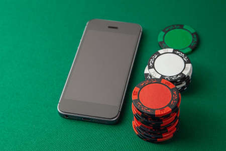 Mobile phone casino online. Mobile phone and chips on green gaming table. Gambling addiction in cracking games. Poker online.の写真素材