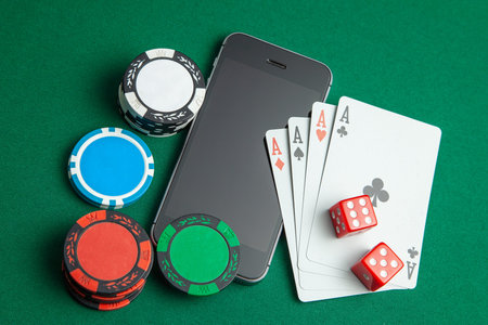 Mobile phone casino online. Mobile phone and game cards with chips and dice on a green gaming table....