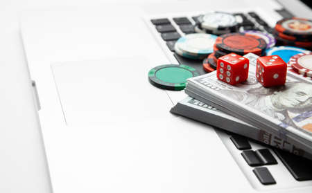 Online casino laptop. Laptop keyboard and chips with dice and money cash dollars on green gaming table. Game addiction gambling. Poker online. Copy space for textの写真素材