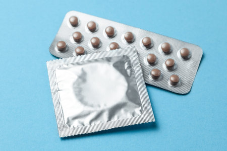 Birth control pills and condom in package on blue background. The concept of choosing method of...