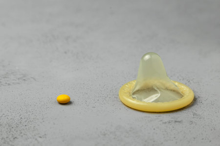 Birth control pills and condom  on gray background. The concept of choosing method of contraception,...