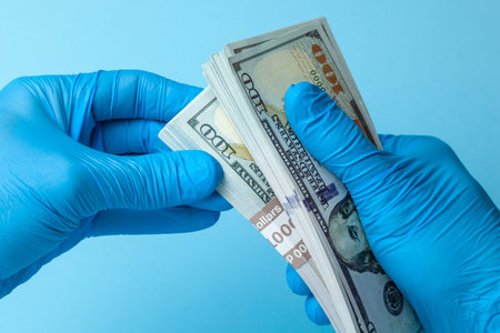 Doctor in blue gloves holds money cash dollars on blue background. Concept of bribe, corruption or...