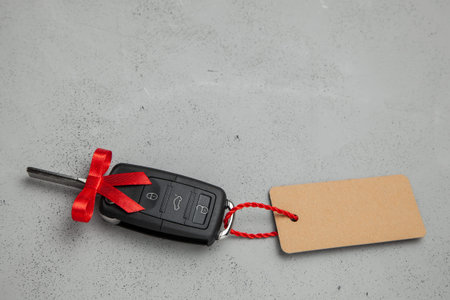 Gift Car keys with remote control alarm with red ribbon with bow and label tag. Gray background....