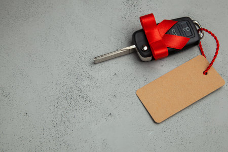 Gift Car keys with remote control alarm with red ribbon with bow and label tag. Gray background. Copy space for textの写真素材