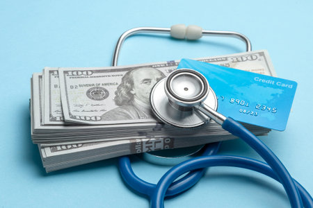 Stack of cash dollars and credit card with stethoscope on blue background. The concept of medical...
