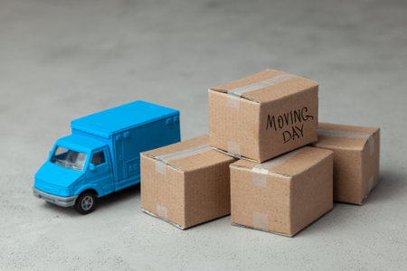 Moving day. Trucking by traveling to a new apartment or office. Paper boxes and truck on gray...
