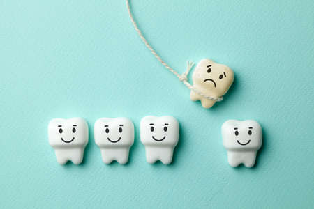 Healthy white teeth are smiling and the removal of the baby tooth with rope is sad on green mint background. Toothbrush and dentist tools mirror, hookの写真素材