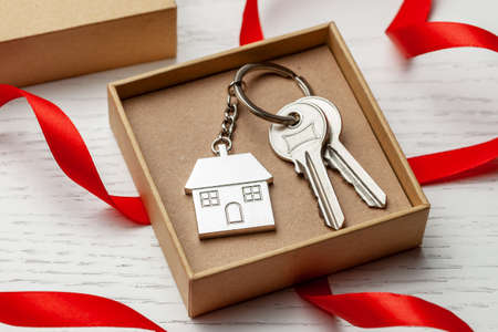 Keychain house and keys with red ribbon and gift box on white wooden backgroundの写真素材