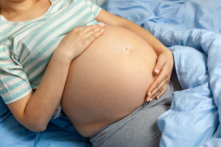 Pregnant woman holding her belly and sitting on the bed