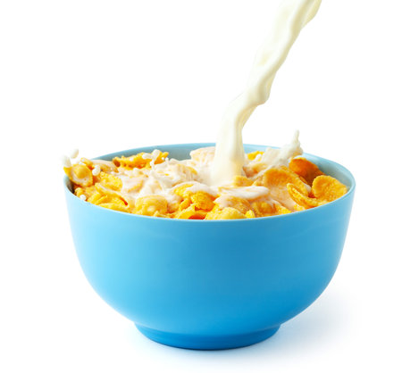 Cornflakes dry breakfast with milk. Stream of milk with cheese and splash pours into blue plate with...