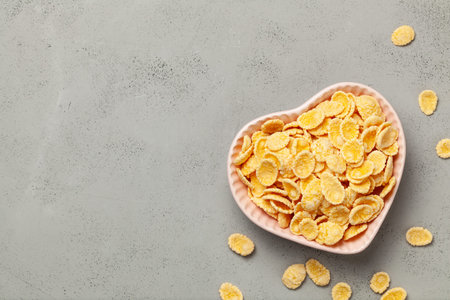 Yellow corn flakes in  heart shaped plate on gray background. I like breakfast cereal. Copy space...