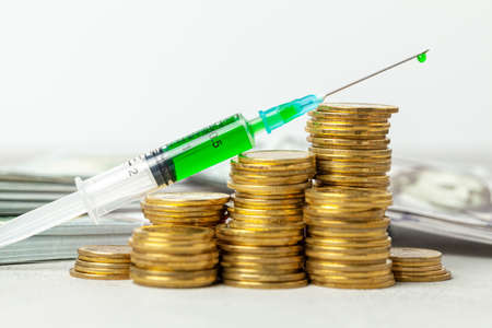 Stack of coins with a ladder growth symbol and syringe with injection. Gray background with banknotes in the backの写真素材