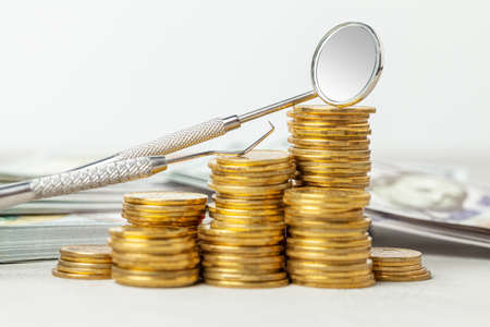 Mirror and hook dentist tools on pile of coins. The concept of expensive dentist or insurance for dentistryの写真素材