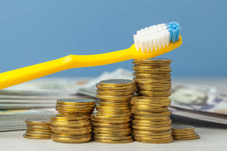 Toothbrush on pile of coins. The concept of expensive dentist or insurance for dentistryの写真素材