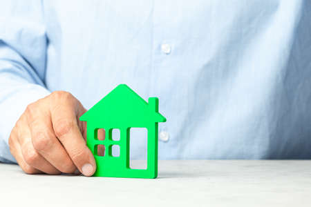 Man in blue shirt holds house in his hands. Concept realtor offers to buy house or real estate loanの写真素材