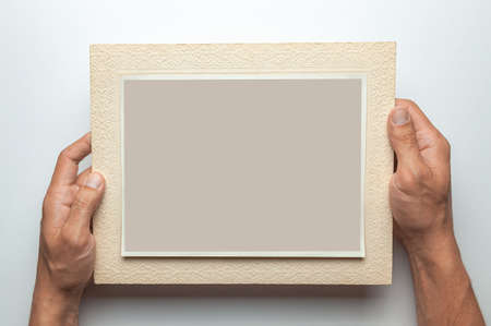 Old photo in frame in the hands of man. Empty template for picture, mock-up. Gray background.の写真素材