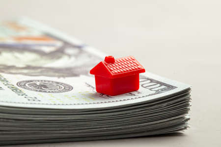 Red house on a stack of money. The concept of insurance or the purchase of real estate.の写真素材