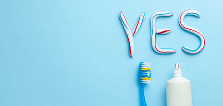 Word YES from toothpaste. Tube of colored toothpaste and toothbrush on blue background. The concept of proper cleaning and care of teeth. Copy space for text.の写真素材