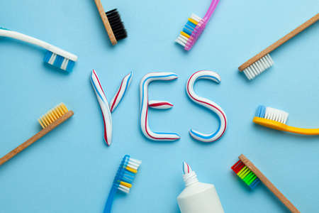 Word YES from toothpaste. Tube of colored toothpaste and toothbrush on blue background. The concept of proper cleaning and care of teeth.の写真素材