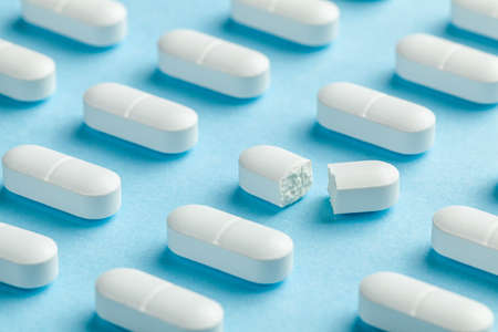 White pills on blue background. One tablet is broken in half, reducing the dose of the medicine.の写真素材
