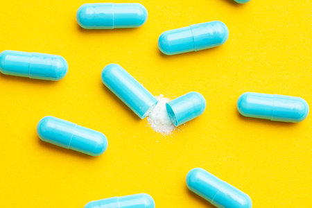 Blue tablets in capsules. One capsule is open. Yellow background.
