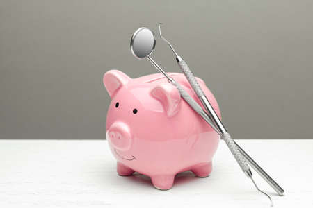 Pink piggy bank and dental tools on gray background. The concept of how to save on dental treatmentの写真素材